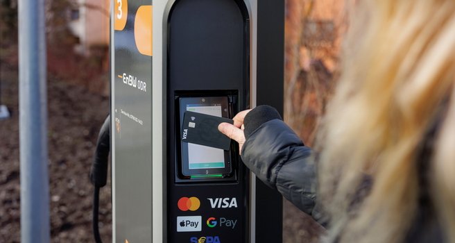 Eine Person hält eine Kreditkarte an das Bezahlterminal einer Ladestation für E-Autos.