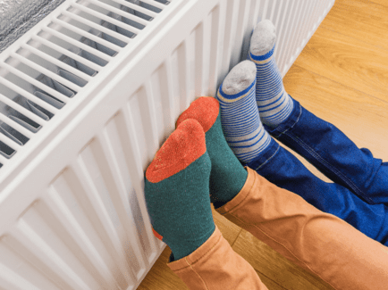 Füße in Socken, die sich an einer neuen Heizung nach einem Heizungstausch erwärmen.