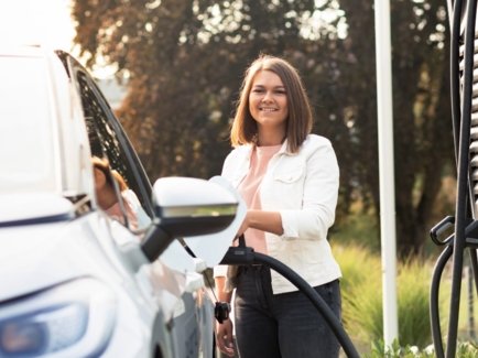 Eine junge Frau steht während des Ladevorgangs vor ihrem Elektrofahrzeug