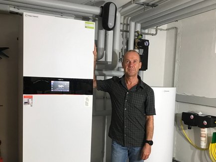 Heizungskunde der Erdgas Südwest steht zufrieden neben seinem neuen Wärmepumpen-Heizsystem im Keller eines Reihenhauses.