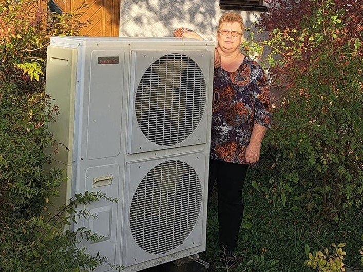 Glückliche Kundin der Erdgas Südwest steht neben Ihrer Wärmepumpe und berichtet von Ihren 18 Jahren Erfahrungen mit Ihrer Wärmepumpe