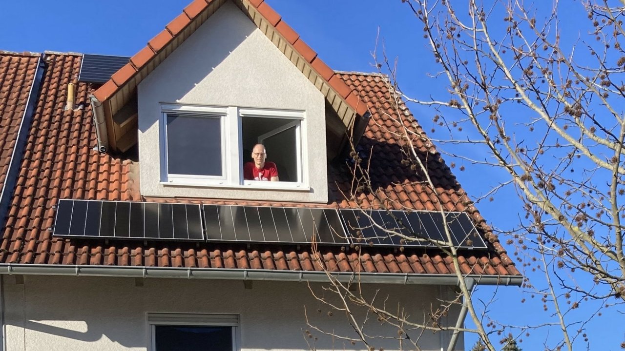 Zufriedener Solarkunde der Erdgas Südwest schaut aus dem Fenster eines Einfamilienhauses