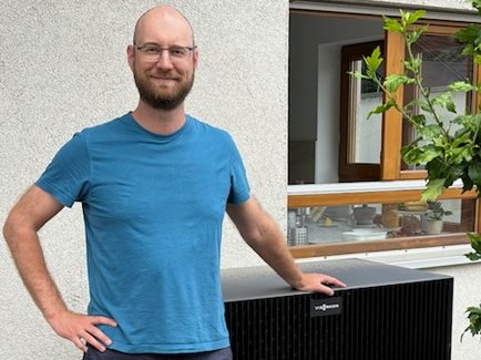 Ein zufriedener Besitzer einer neuen Wärmepumpe aus Karlsruhe vor seinem Wärmepumpen-Außengerät stehend.