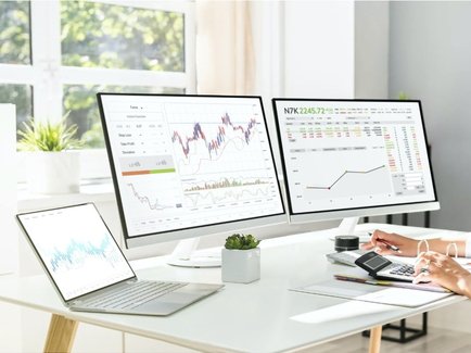 Eine am Schreibtisch sitzende Unternehmensmitarbeiterin beobachtet und kalkuliert die Energie-Börsenpreise.