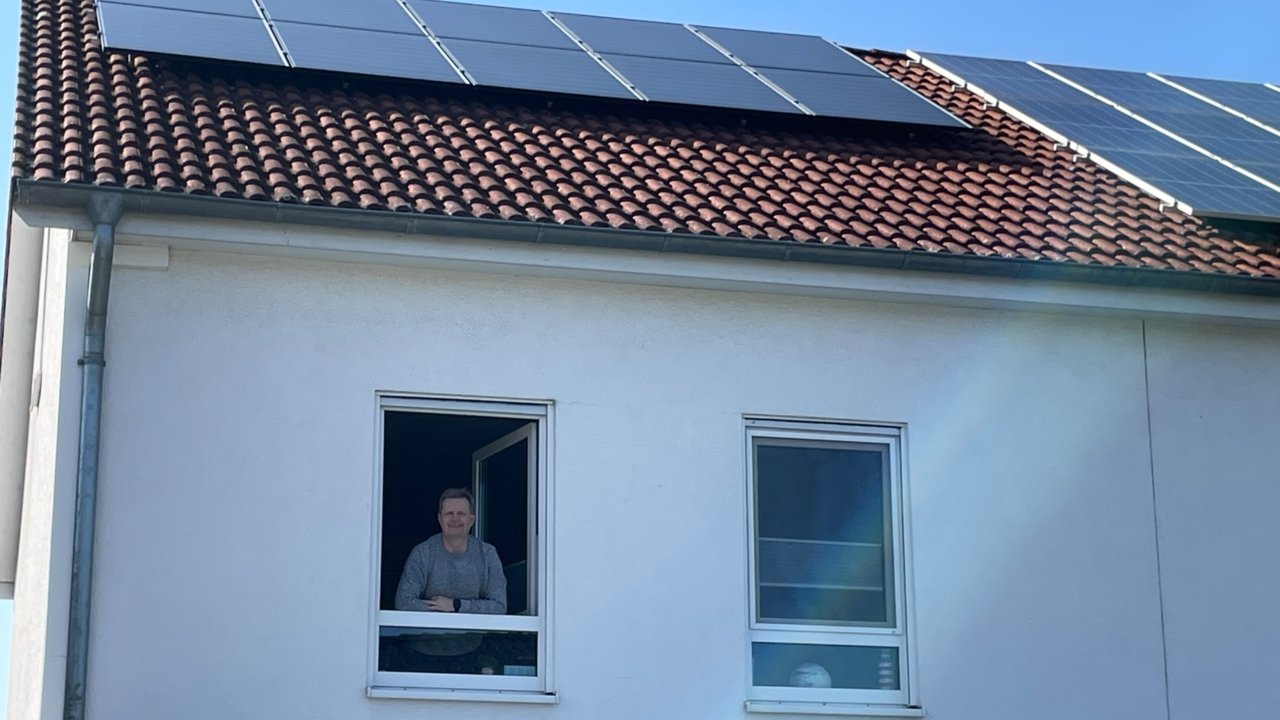 Zufriedener PV-Kunde der Erdgas Südwest schaut aus dem Fenster eines Einfamilienhauses