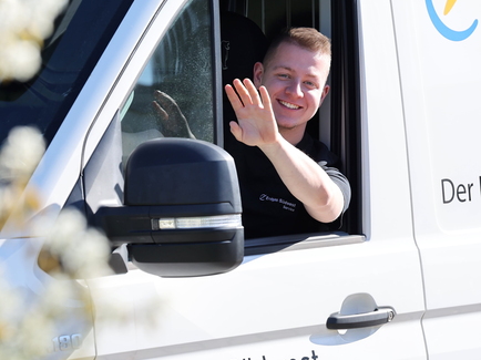 Ein freundlicher Heizungsmonteur winkt aus dem Serviceauto heraus nach erfolgreicher Installation der neuen Wärmepumpe.