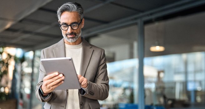 Erfahrener Geschäftsmann nutzt im Büro ein Tablet für Analyse und Beratung.