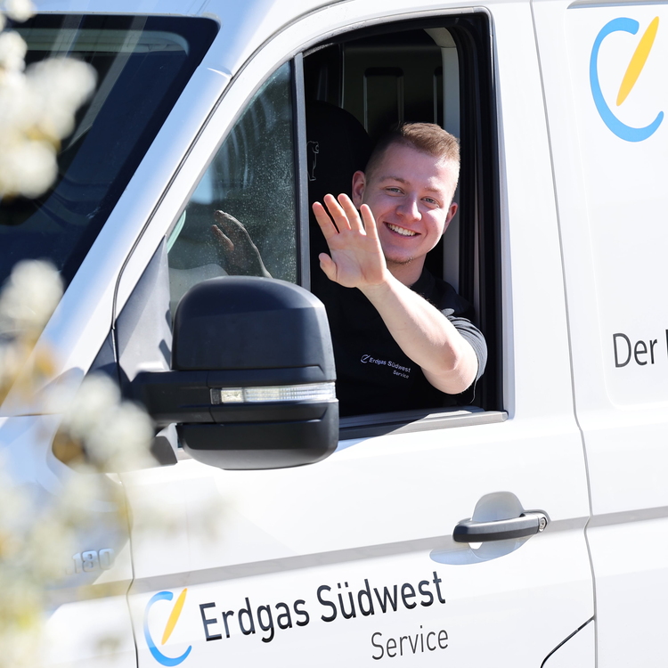 Ein freundlicher Heizungsmonteur winkt aus dem Serviceauto heraus nach erfolgreicher Installation der neuen Wärmepumpe.