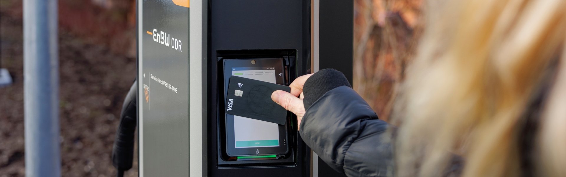Eine Person hält eine Kreditkarte an das Bezahlterminal einer Ladestation für E-Autos.