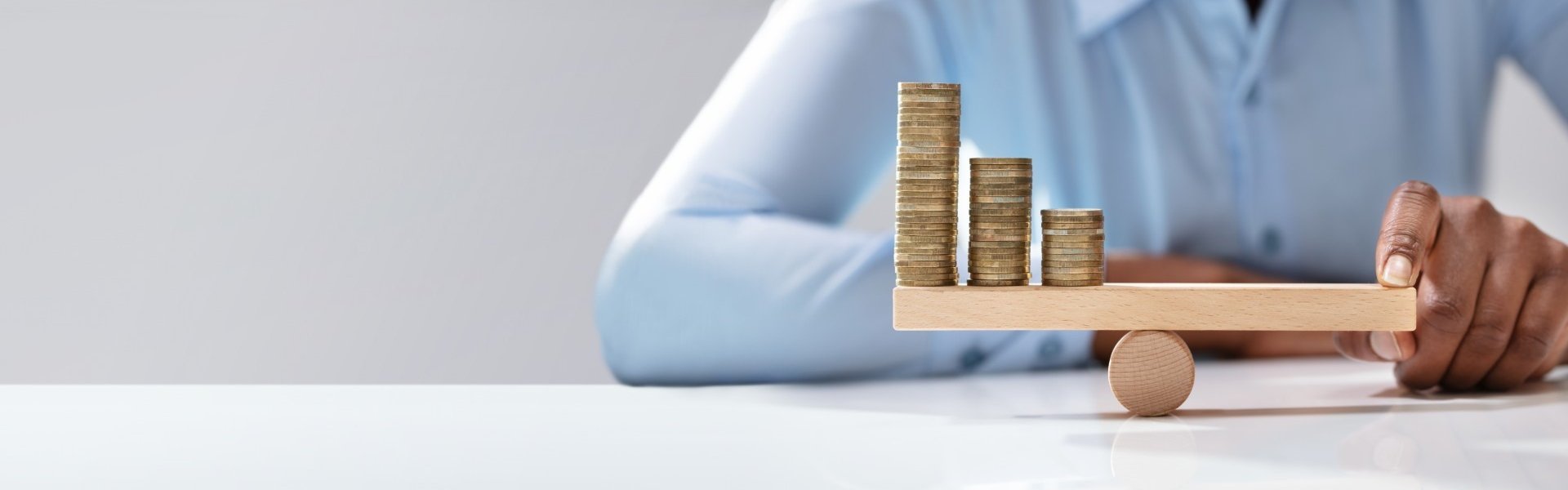 Businessfrau sitzt an einem Schreibtisch und balanciert Geldmünzen auf einer Art Wippe aus.