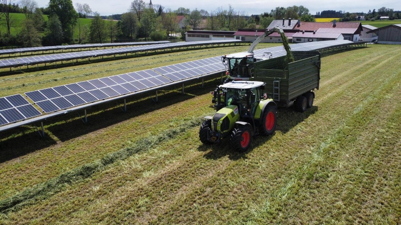 Landwirtschaftliche Traktoren fahren  auf einer Agrarfläche neben einer PV-Anlage, für die die Batteriespeichervermarktung eingesetzt wird.
