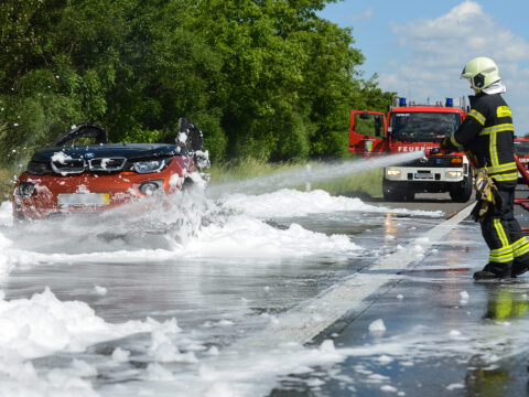 Feuerwehr löscht mit Schaum ein brennendes Elektroauto auf der Autobahn