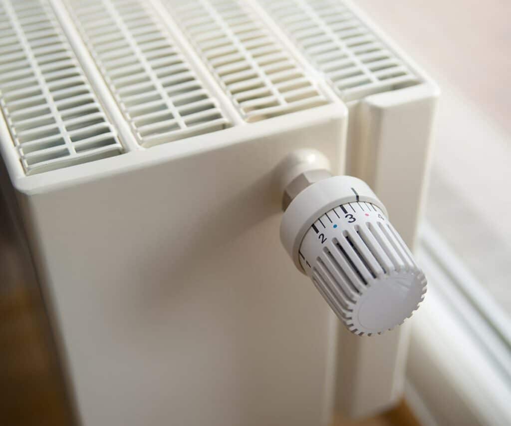 Ausschnitt Konvektor Heizkörper mit Thermostat vor einem Fenster