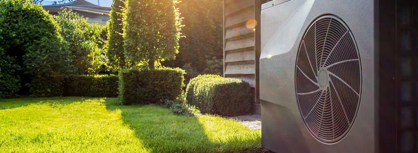 Außengerät einer Wärmepumpe mit Ventilator in einem grünen Garten vor einem Haus