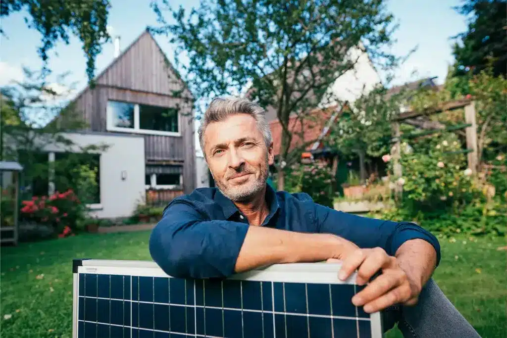 Mann mit Solarpanel vor Eigenheim