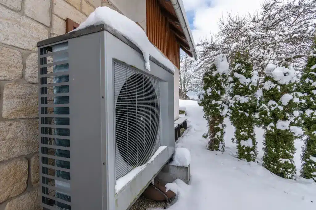 Schneebedeckte Wärmepumpe vor Haus